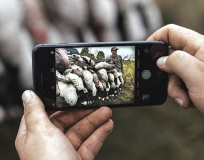A goose hunter takes a photo with his cell phone for social media.